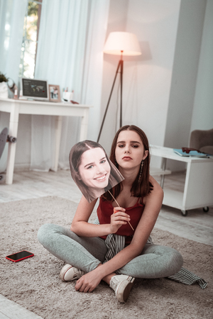 Having a mask. A girl hiding her sadness behind a false smileの写真素材