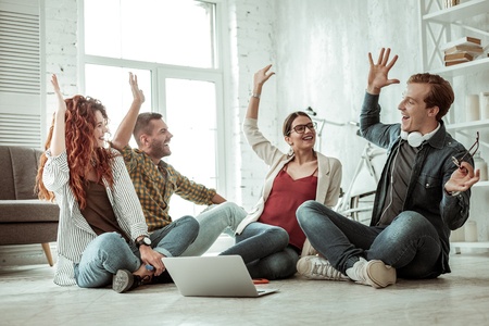 We are the team. Delighted positive people giving each other high five while sitting together on the floorの写真素材
