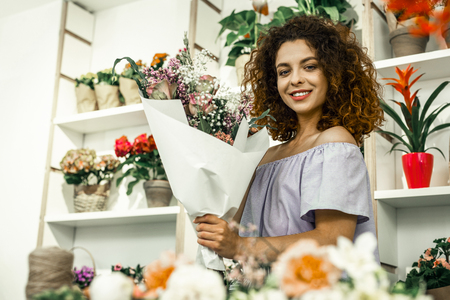 Showing bouquet. Professional young florist showing amazing bouquet while standing in floral shopの写真素材