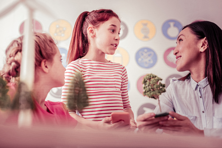 Young ginger girl. Long-haired pretty girl excitedly discussing current topic of the lesson with teacher and friend nearbyの写真素材