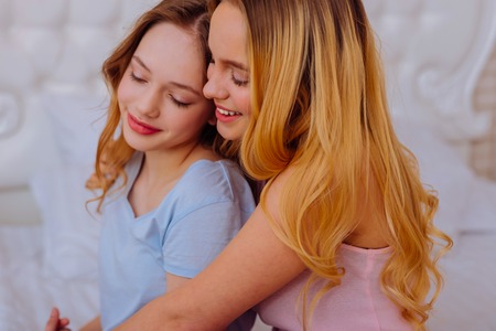 Older sibling. Younger sister feeling supported and happy with her older sibling while hugging each otherの写真素材