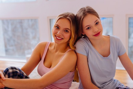 Day together. Two beaming appealing sisters feeling amazing spending day together at homeの写真素材