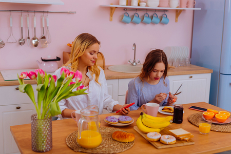 Enjoying breakfast. Two sisters enjoying breakfast at home eating some sweet doughnuts and drinking juiceの写真素材