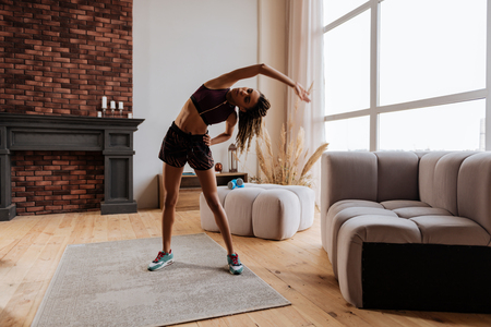 Stretching body. Fit active woman wearing shorts stretching her body after finishing workout at homeの写真素材