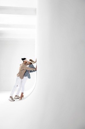 In white room. Two professional models wearing white trousers posing for brand promotion in white...