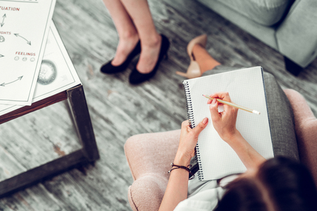 Holding pencil. Top view of psychologist wearing nice bracelet holding pencil while making notesの写真素材