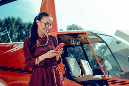 Checking smartphone. Beaming good-looking lady in clear glass being contented with her smartphone...