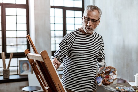 Light workshop. Bearded professional artist wearing glasses working in light spacious workshopの写真素材