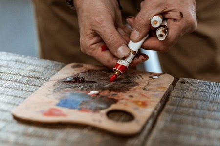 Red gouache. Close up of experienced male artist putting some red gouache on little wooden boardの写真素材