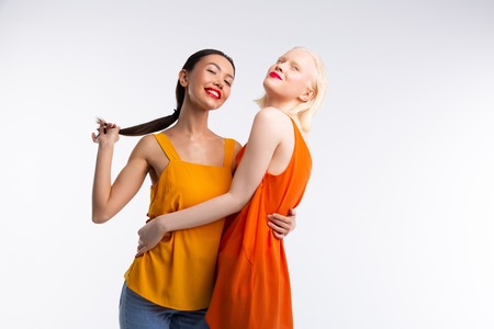 Women hugging. Women with red lips wearing bright blouses hugging while posing near white backgroundの写真素材