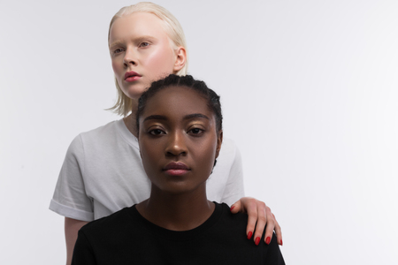 Standing behind. Woman with blonde bob cut standing behind African-American woman