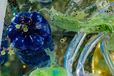 Causing global warming. Blue used plastic bottle immersed in dirty water with colorful harmful garbageの写真素材