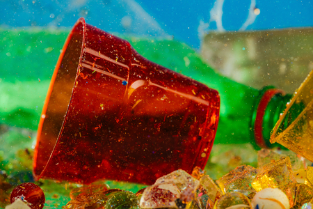 Disposal colorful plastic. Red transparent cup lying on the water bottom with plastic pieces underの写真素材