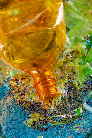 Lying in trash. Orange opened bottle made of non-decomposed plastic being surrounded with glitter piecesの写真素材