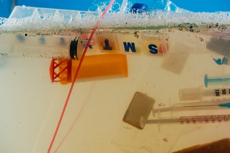 Muddy dirty water. Heap of plastic syringes placed in transparent bag and floating in soapy water