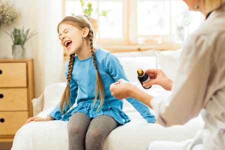 Refusing to take medicine. Little ill mischievous long-haired girl yelling at hospital and refusing to take a medicine offered by a doctorの写真素材