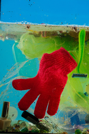 Woolen red glove. Thrown red glow floating in polluted water with plastic pieces and glitter flakesの写真素材