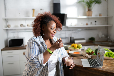 Cooking blog. Delighted female keeping smile on her face while looking at her laptopの写真素材