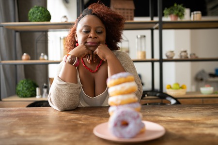 Dreamy mood. Delighted housewife pressing lips while looking at doughnutsの写真素材
