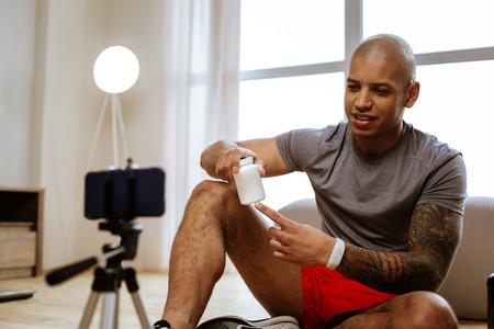 Blog about diet. Young strong sportsman with tattoo on his hand filming blog about dietの写真素材