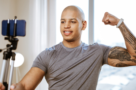 Photo of biceps. Handsome strong sportsman making photo of his biceps on the smartphoneの写真素材