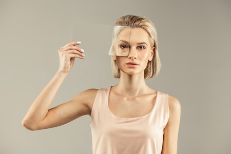 Aging process. Nice young woman putting a mirror to the eye while seeing the aging processの写真素材