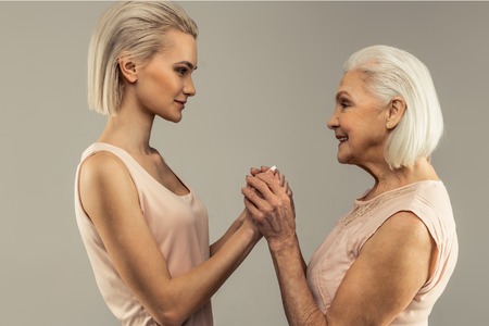 Special connection. Pleasant nice women holding each others hands while standing opposite each other