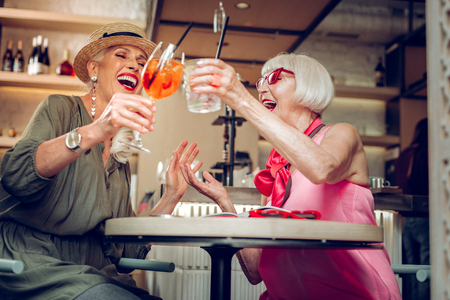Low angle of positive happy women cheering with drinks while sitting together in the cafeteriaの写真素材