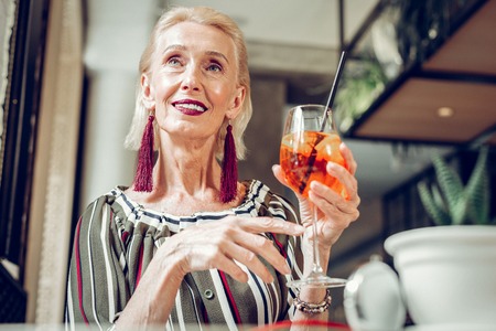 Pleasant relaxation. Joyful dreamy woman drinking aperol while resting in the restaurantの写真素材