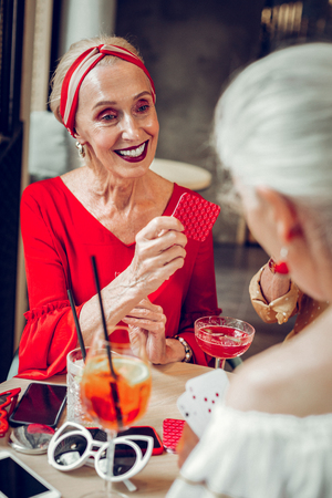 Nice joyful woman looking at her friend while playing cards with herの写真素材