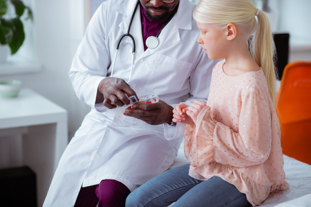 Vitamins for girl. Close up of pediatrician wearing white coat giving stylish girl vitaminsの写真素材