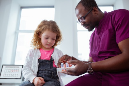 Cute curly girl. Cute little curly girl taking pills from pleasant pediatrician wearing uniform