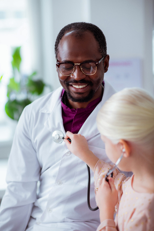 Day with daughter. Dark-skinned pediatrician feeling happy while spending day with daughter at his workの写真素材