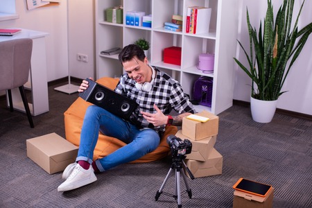 Pointing on speaker. Active involved video blogger sitting in orange bag chair and creating review of music deviceの写真素材