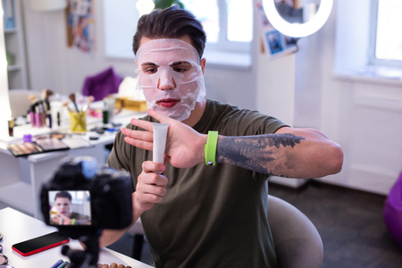 Educating followers. Resolute experienced beauty blogger reviewing new cosmetic product in white tube with recording itの写真素材