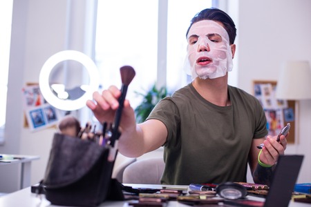 Showing drawing techniques. Unusual beauty artist sitting in bright studio and taking makeup brush from filled pileの写真素材