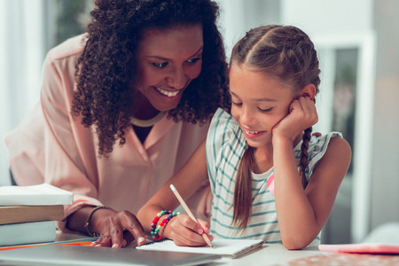 Helping with a homework. Charming alluring loving bewitching dark-haired Afro-American mother in...