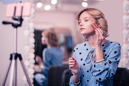 Using dark concealer. Blonde beauty blogger using dark concealer while making video blogの写真素材