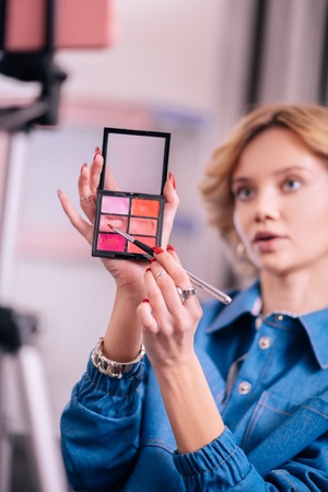 Lip gloss palette. Young beauty blogger in denim jacket showing lip gloss palette on cameraの写真素材