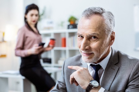 Having unpleasant smile . Shameless beaming old man pointing on dark-haired woman while she staying behindの写真素材