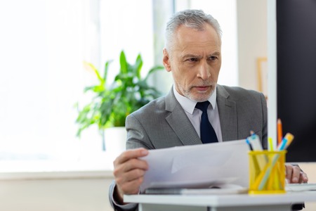 Bright spacious office. Concerned short-haired old office worker being confused with information on the screen while workingの写真素材