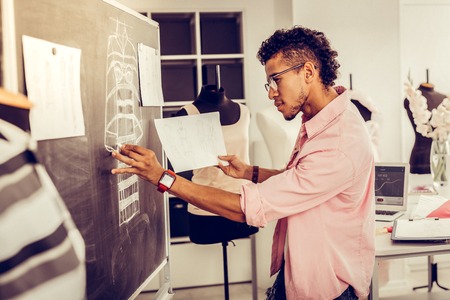 Working intently. Young focused fashion designer enthusiastically redrawing his sketch from a sheet...