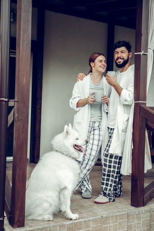 Morning in family circle. Beaming smiling glowing happy mid-adult spouses wearing pajamas standing near doors with coffee in hands.の写真素材