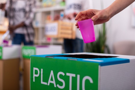 Pink glass. Close up of girl putting pink glass into box with plastic while sorting wasteの写真素材