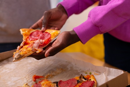 Pizza with salami. Dark-skinned teenager in purple sweatshirt holding pizza with salami