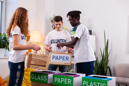 Sorting waste. Three teenagers wearing jeans and white t-shirts sorting waste separating paper from plasticの写真素材