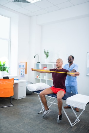 Stretching arms. Young bald bodybuilder stretching his arms while visiting sports therapist