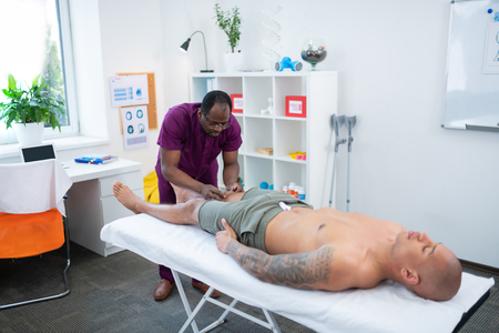 Sportsman closing eyes. Tattooed sportsman closing his eyes while enjoying rehabilitation massageの写真素材
