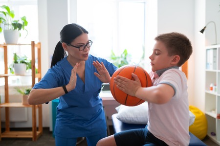 Pushing hands. Active dark-haired nurse in blue uniform showing example of exercise with ball