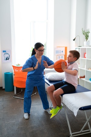 Exercise with ball. Helpful Asian physical therapist working with little boy while he developing...